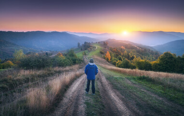 Wall Mural - man on the dirt road on the hill and mountains in fog at colorful sunset in autumn in ukraine. lands