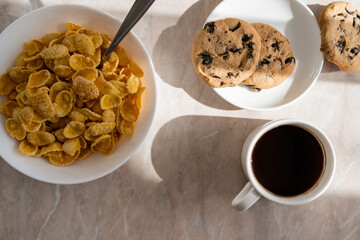 Wall Mural - top view of cup of black coffee near chocolate chip cookies and bowl with corn flakes on marble surface.