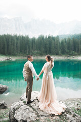 Wall Mural - Young couple near lake Karersee, Italy. Holding hands at the stone at lake