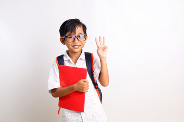 Happy asian schoolboy standing while showing three fingers, carrying a book and school bag