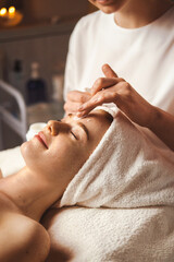 Wall Mural - beautician applying facial cream all over young woman's forehead at spa salon. skin treatment. girl 