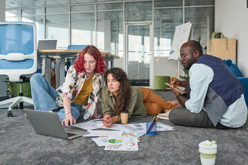 Poster - Group of employees gathered in front of laptop discussing data at meeting while one of them making notes in notepad