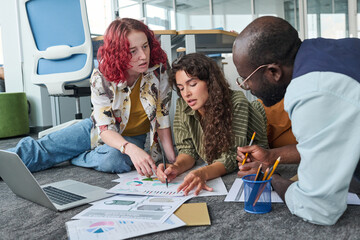Poster - Two young confident women pointing at financial document while one of them explaining graphic data to male colleague during discussion