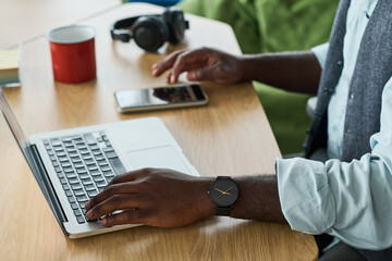Aufkleber - Hands of young black man in formalwear keeping hand over laptop keypad while scrolling in smartphone on workplace