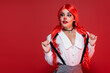 young redhead woman in halloween makeup touching suspenders and looking way isolated on red.