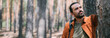© Anna - Portrait of a young man with a backpack on a walk in a pine forest on a sunny day. The guy breathes fresh air in a coniferous forest