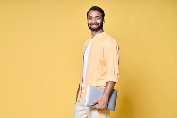 Smiling happy confident indian man standing isolated on yellow background holding laptop advertising web products for job search, elearning trainings promotion, presenting online business education.