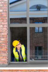 Sticker - construction business and building concept - smiling male builder in helmet and safety west looking out window