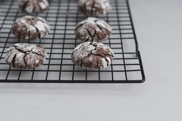 Angle view shot food photo of freshly baked Chocolate Crinkle Cookies. Chocolate iced biscuits arranged on black wire cooling rack. White work surface background. Copy space available