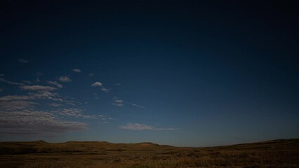 Wall Mural - moonlit clouds move quickly through a sky with stars in a time lapse above a peaceful fall prairie s