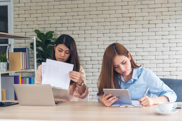 Wall Mural - Two businesswomen team meeting using laptop at company office desk. Two young Female freelance reading financial graph charts Planning analyzing marketing data. Asian people team working office firm.