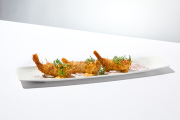 Wall Mural - Traditional greek appetizer - kataifi wrapped shrimps on white plate. Crispy shrimp in kataifi crust in summer day. Shrimp appetizer fried in kataifi dough. Crispy prawns in modern style.