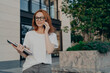 © VK Studio - Thoughtful redhead woman looks into distance makes phone call holds smartphone near ear
