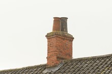 Close-up Shot Of Two Weathered Chimney Pots On A Brick Chimney Stack With A Background Of The Sky