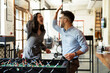 © JustLife - Colleagues having fun at work. Businessman and businesswoman playing table soccer.