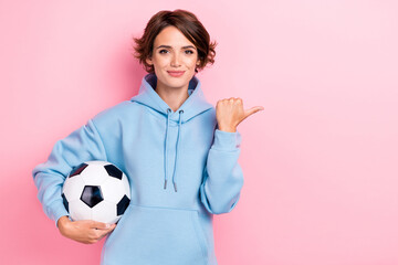 Sticker - Photo of young adorable gorgeous nice pretty girl wear blue hoodie hold football ball finger pointing empty space positive recommend isolated on pink color background