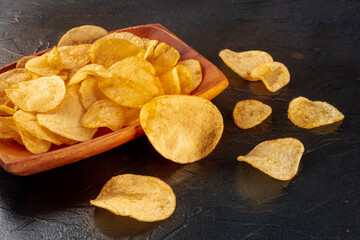 Poster - Potato chips or crisps in a bowl and scattered on a black stone background, a close-up