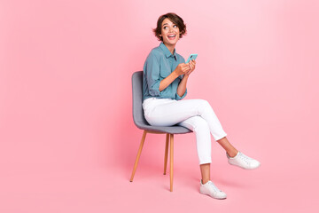 Canvas Print - Photo of funny lady trendy outfit sit chair look interested empty space hand hold use telephone gadget isolated on pink color background