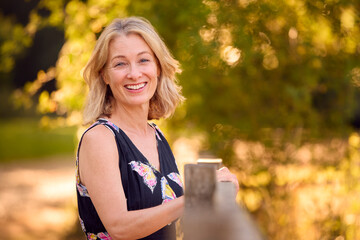 Portrait Of Casually Dressed Mature Woman Leaning On Fence On Walk In Countryside