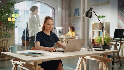 Poster - Beautiful Female in a Black Casual Dress Sitting at a Desk in Creative Office, Working on Tasks on Laptop Computer. Smiling Creative Specialist Writing Corporate Project Plans for Marketing Agenda.