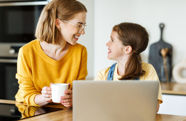Fototapete - Cheerful girl using a laptop with  her mom    in the kitchen at home