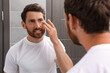 © New Africa - Handsome bearded man looking at mirror in bathroom