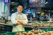 portrait of a happy handsome Asian salesman. Vegetables and fruits at the market or grocery store. Seller. a man in an apron looks at the camera and smiles farmer, small business owner greengrocer