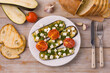Plate of grilled eggplant with feta cheese and grilled tomatoes on a white wooden background, top view.