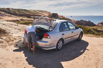 Wall Mural - Man taking sport clothes out from the trunk while standing outside with surfboards