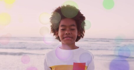 Poster - Animation of colourful light spots over smiling african american girl on beach by sea at sundown