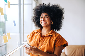 Wall Mural - Happy black businesswoman using a smartphone in a creative office