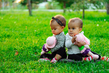 Twin Babies Playing With Doll And Sitting On The Lawn Outside