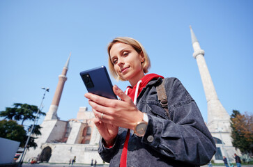 Wall Mural - Enjoying vacation in Istanbul. Young traveling woman using smartphone near Hagia Sophia Temple.