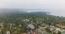 Beautiful Green Inhabited Shore Of Pacific Ocean In Carmel-by-the-Sea, California. Coastline Panorama Covered With Slight Fog From Top. Hazy Horizon At Backdrop.