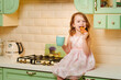 © andrey - a cheerful little girl drinks cocoa with gingerbread in the kitchen.