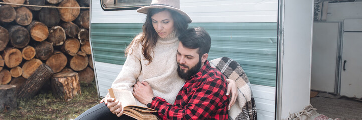 Wall Mural - Young beautiful loving couple travelling across country in the van. Millennial man and woman in a travel camper. Cozy atmosphere, vacations vibe. Banner copy space