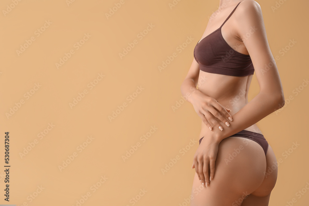 Slim young woman in underwear on beige background