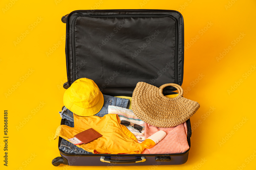 Suitcase with clothes, beach accessories, ticket and passport on yellow background