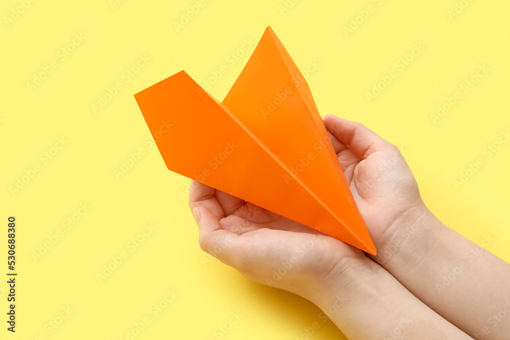 Woman with orange paper plane on yellow background, closeup