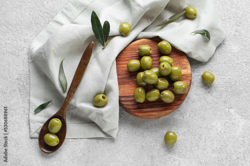 Wooden board with tasty green olives on light background