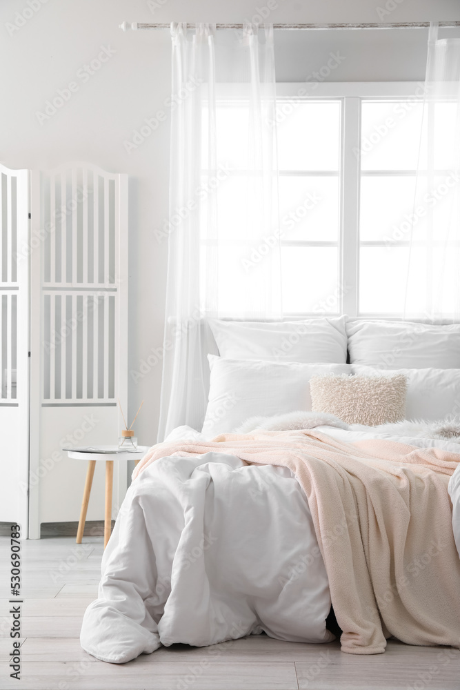 Interior of light room with big bed, table and folding screen