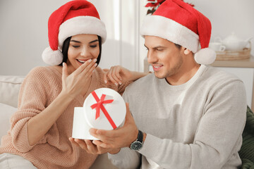 Poster - Happy young couple with Christmas gift sitting on sofa in living room