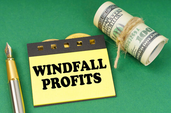 On a green surface are a pen, dollars and yellow stickers with the inscription - Windfall profits
