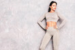 © halayalex - Fitness confident woman in sports clothing. Sexy young beautiful model with perfect body. Female posing near grey urban wall in studio. Stretching out before training