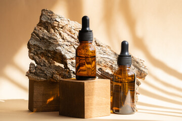 Wall Mural - Two amber glass bottles with facial serum in sunlight on wooden 3d podium. Packaging for cosmetics with dropper lid, containers for liquids, essential oils next to bark of tree on brown background