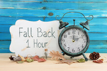 Image Of Autumn Time Change. Fall Back Concept. Dry Leaves And Vintage Alarm Clock On Rustic Wooden Table