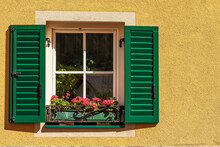 Close-up Of A Window With Green Wooden Shutters And Red Geranium Flowers. Small Village Of Malborghetto-Valbruna In Val Canale, Udine Province, Friuli-Venezia Giulia, Italy, Europe.