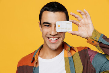 Poster - Close up young smiling happy fun middle eastern man 20s he wear casual shirt white t-shirt hold in hand mock up of credit bank card isolated on plain yellow background studio People lifestyle concept.