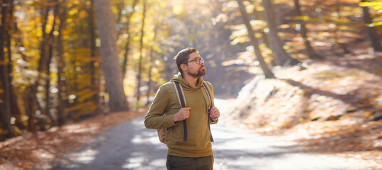 Wall Mural - Young handsome man posing in autumn forest. young hipster guy with backpack , traveller standing in woods, Hiking, Forest, Journey, active healthy lifestyle, adventure, vacation concept.