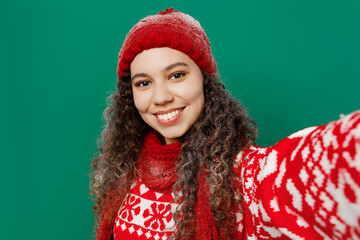 Sticker - Close up merry young woman in red warm cozy knitted sweater hat posing do selfie shot pov on mobile cell phone isolated on plain dark green background Happy New Year 2023 celebration holiday concept